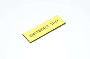 Merkkikilpi, keltainen, 60,5x20mm suorakulmainen, "EMERGENCY STOP"